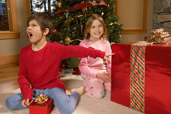 a young boy pointing angrily at his smiling sister and her gift