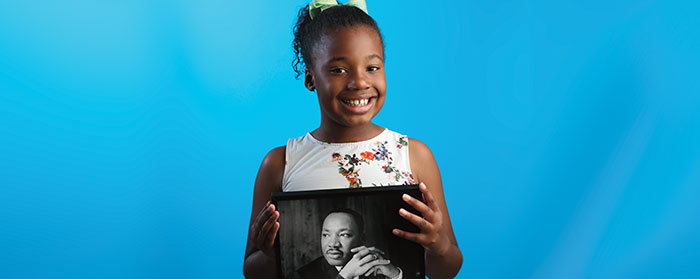 A smiling girl holding a picture of Martin Luther King Jr.