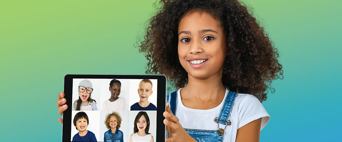 A girl smiling holding an iPad of six other kids smiling