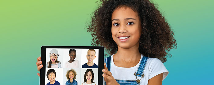 A girl smiling holding an iPad of six other kids smiling